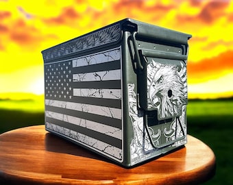 May include: A dark green metal ammo box with a distressed American flag design on one side and an eagle graphic on the other. The box is on a wooden table with a sunset background.