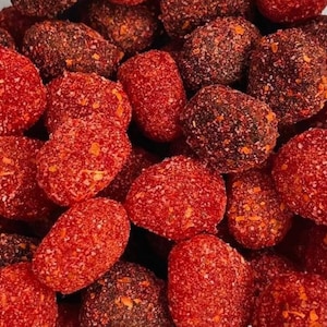 Puede incluir: Primer plano de un bol lleno de caramelos cubiertos de azúcar rojo y rojo oscuro. Los caramelos son redondos y tienen una superficie ligeramente texturizada.