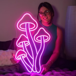 A woman holding a purple and pink led neon sign depicting mushrooms.