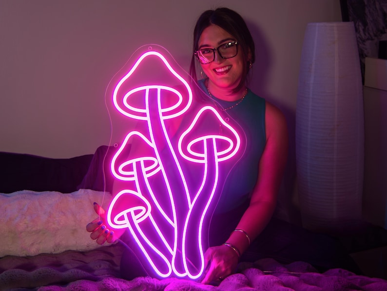 A woman holding a purple and pink led neon sign depicting mushrooms.