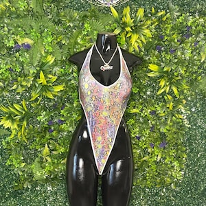Può includere: Un body sgambato caratterizzato da un motivo multicolore a pelle di serpente nei toni del rosa, giallo, viola e arancione con bordi bianchi. Una collana a catena color argento con un ciondolo che recita "Queen" in corsivo poggia sullo scollo.