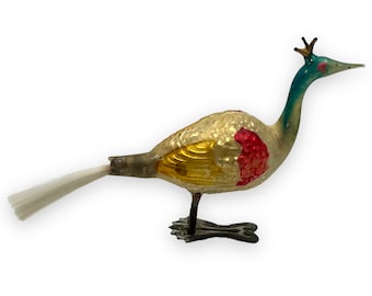 May include: A vintage glass Christmas ornament shaped like a bird with a white feather tail. The bird is painted gold, yellow, red, and blue.