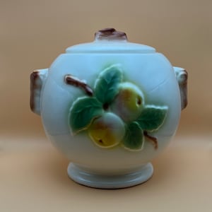 May include: White ceramic cookie jar with a lid and two handles. The jar is decorated with a brown branch with green leaves and three yellow apples.