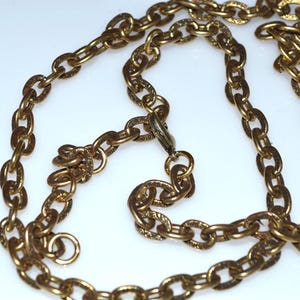 May include: A vintage gold-toned chain necklace with oval links. The links have a textured pattern and are connected with a clasp. The necklace is displayed on a white surface.