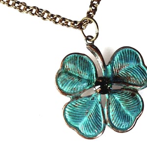 May include: A bronze-toned necklace featuring a four-leaf clover pendant with a distressed teal finish. The clover has a dark center stone and is suspended from a matching chain, creating a vintage-inspired accessory.