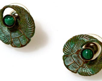 May include: A pair of green and gold earrings featuring a scarab beetle design with a malachite stone in the center.