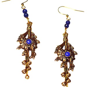 May include: A pair of gold-toned earrings with a floral design and blue gemstone accents. Each earring features a cluster of leaves and a central blue stone, with a series of small beads and a hook for pierced ears. The earrings are designed to dangle.