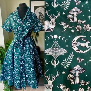 May include: A green dress with a white print of woodland creatures, moons, stars, and other nature-inspired designs. The dress has a collared neckline, short sleeves, and a button-up front.