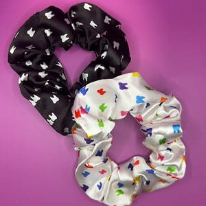 Puede incluir: Dos coleteros con temática dental. Uno es negro con dientes blancos, y el otro es blanco con dientes coloridos. Los coleteros son de tela brillante, sobre un fondo morado.