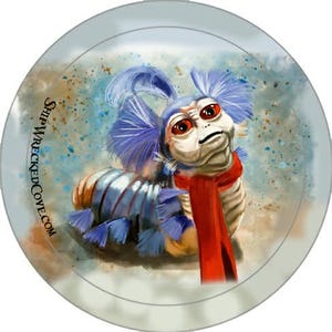 May include: A circular button featuring a digital illustration of a caterpillar-like creature with large orange eyes, blue feathery antennae, and a bright red scarf. The text SHIPWRECKEDCOVE.COM is printed vertically along the left side of the image.