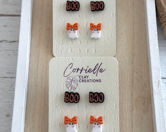 Könnte beinhalten: Zwei Paar Halloween-Ohrringe. Das erste Paar zeigt einen schwarzen und orangefarbenen "BOO"-Anhänger und einen weißen Geist mit einer orangefarbenen Schleife. Das zweite Paar zeigt einen schwarzen und orangefarbenen "BOO"-Anhänger und einen weißen Geist mit einer orangefarbenen Schleife. Die Ohrringe werden auf einer weißen Karte mit dem Text "Corrielle Clay Creations" präsentiert.