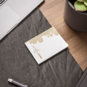 May include: A white notepad with a gold sword design and a pattern of concentric circles at the top. The notepad is on a gray textured surface.