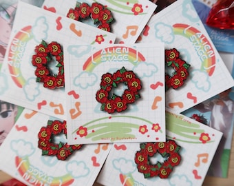 Peut inclure: Épingles en émail représentant une couronne de fleurs rouges. Les épingles sont présentées sur des cartes avec le texte "Alien Stage" et un arc-en-ciel. Le fond comprend des notes de musique et des fleurs.