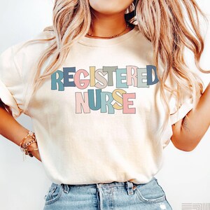 May include: A white t-shirt with the text "REGISTERED NURSE" in colorful block letters. The letters are outlined in black and filled with different pastel colors.