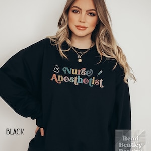 May include: Black sweatshirt with a colorful retro graphic that says "Nurse Anesthetist" with a stethoscope and syringe.