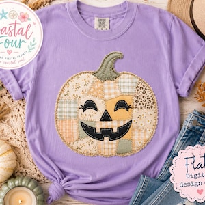 May include: A light purple short-sleeve t-shirt featuring a large, central pumpkin graphic. The pumpkin is composed of various beige, cream, and sage green fabric patches with floral, plaid, and leopard print patterns, finished with a black jack-o'-lantern face.
