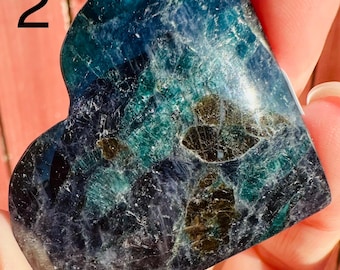 May include: A heart-shaped polished stone featuring a deep blue and teal color palette with dark brown inclusions. The surface displays a crystalline texture with visible internal fractures and a glossy finish. The number 2 is visible.