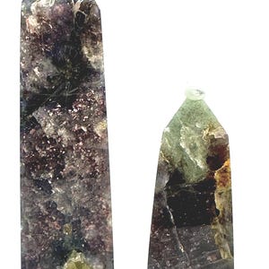 May include: Two polished crystal obelisks. The larger obelisk is a dark purple and gray color with flecks of gold and green. The smaller obelisk is green, brown, and purple. Both have a clear crystal tip.