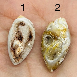 May include: Two natural stone pendants, numbered 1 and 2. Pendant 1 is white with a brown interior, while pendant 2 is a mix of white, yellow, and brown. Both are teardrop-shaped and appear to be geode slices.