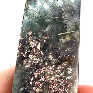 May include: A tall, rectangular crystal obelisk with a polished surface. The stone features a dark, mottled base color with areas of pink and white speckling. Thin, white lines run through the stone.