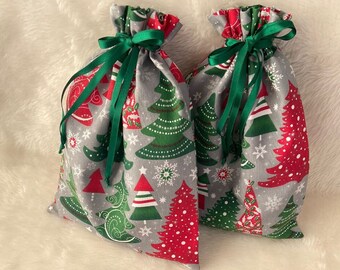 May include: Two gray Christmas gift bags with green ribbon ties. The bags are decorated with a repeating pattern of red and green Christmas trees and snowflakes.