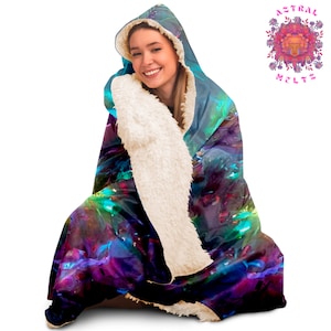 K&ouml;nnte beinhalten: Eine Kapuzendecke mit einem farbenfrohen, abstrakten Design in Blaut&ouml;nen, Lila, Gr&uuml;n und Rosa. Die Decke ist aus weichem, pl&uuml;schem Stoff gefertigt und hat ein wei&szlig;es Sherpa-Futter.