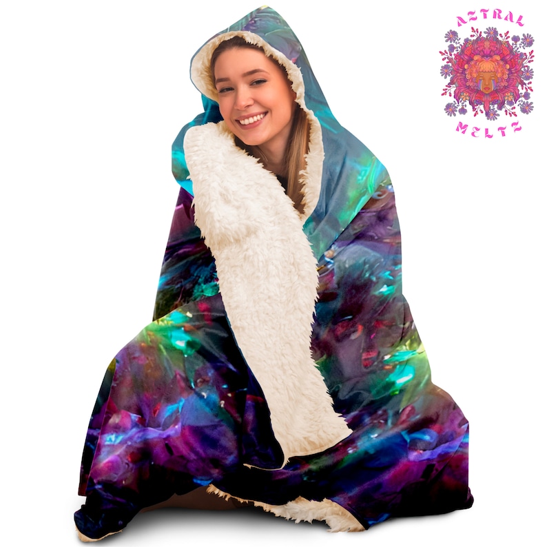K&ouml;nnte beinhalten: Eine Kapuzendecke mit einem farbenfrohen, abstrakten Design in Blaut&ouml;nen, Lila, Gr&uuml;n und Rosa. Die Decke ist aus weichem, pl&uuml;schem Stoff gefertigt und hat ein wei&szlig;es Sherpa-Futter.