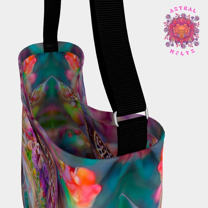 May include: A colorful tote bag with a floral pattern and a black adjustable strap. The bag has a large opening and is made of a soft, durable fabric.