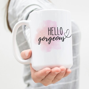 May include: White ceramic mug with a pink watercolour design and the text "Hello gorgeous" in black lettering with a small heart.
