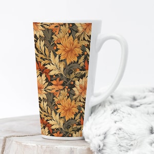 May include: Tall white ceramic mug featuring a floral pattern in shades of orange, gold, and brown. The design includes stylized flowers and leaves against a dark background. The mug has a curved handle and a smooth, glossy finish.
