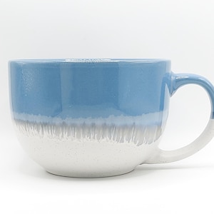 May include: A large ceramic mug with a blue and white gradient design. The top half is a solid light blue, transitioning to a gray band, and then to a speckled white base. The handle is white with a blue accent.