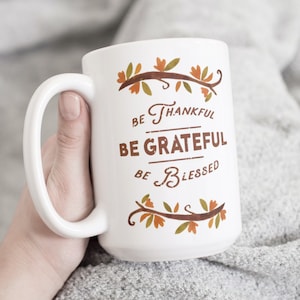May include: White ceramic coffee mug with a brown and orange autumn leaf design and the text "Be Thankful, Be Grateful, Be Blessed".
