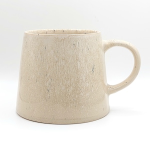 May include: A ceramic mug with a tapered silhouette and a wide base. The exterior features a light beige, speckled glaze with a subtle vertical texture. It includes a single curved handle on the right side and a smooth, rounded rim at the top.