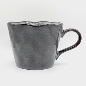 May include: A dark gray ceramic mug with a glossy finish and a scalloped, wavy rim. The mug features a tapered body that widens toward the top and a curved handle on the right side. The surface has subtle variations in tone and texture.