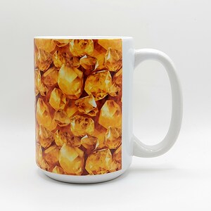 May include: White ceramic mug with a design of golden yellow gemstones. The mug has a large handle.