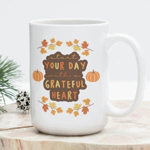 May include: White ceramic mug with a large handle. The mug features the text "Start Your Day with a Grateful Heart" in brown and orange, with leaf and pumpkin illustrations. A perfect gift for autumn.