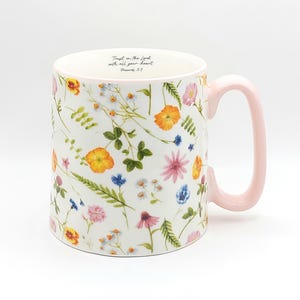 May include: White ceramic mug with a floral pattern of colorful flowers and green leaves. The mug has a light pink handle and the text "Trust in the Lord with all your heart. Proverbs 3:5" printed inside the rim.