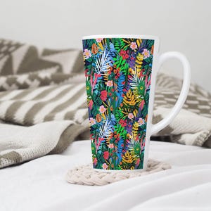 May include: A tall white mug with a colorful floral pattern featuring green leaves, pink, yellow, and red flowers. The mug has a black handle.