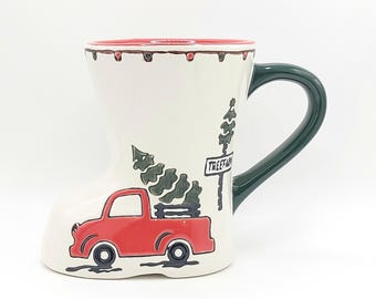 Pode incluir: Caneca de cerâmica branca em forma de bota, com um caminhão vermelho transportando árvores de Natal. A caneca tem uma alça verde e uma borda vermelha. As palavras "Tree Farm" estão em uma placa.