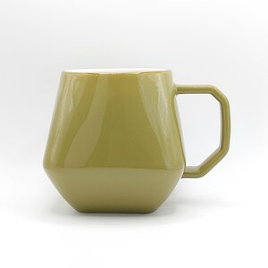 May include: A green ceramic mug with a geometric shape and a white interior. The mug has a handle and a glossy finish.