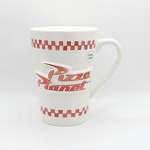 May include: White ceramic mug with a large handle, featuring the Pizza Planet logo in red. The mug has a red and white checkered pattern around the top and bottom. The words "DOUBLE SIDED" are printed on the side.