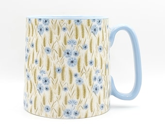 May include: A ceramic mug with a light blue handle and rim. The mug features a repeating pattern of blue flowers and wheat stalks on a cream background. The mug is designed for hot beverages.