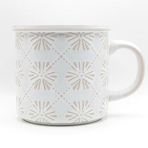May include: White ceramic mug with a beige floral pattern and a rounded handle. The mug features a repeating design of stylized flowers within a diamond grid. The rim and the interior of the mug are beige.