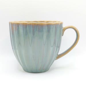 May include: A ceramic mug with a ribbed design in shades of blue and green, featuring a golden-brown rim and handle. The mug has a glossy finish and is set against a white background. Ideal for tea, coffee, or other hot drinks.