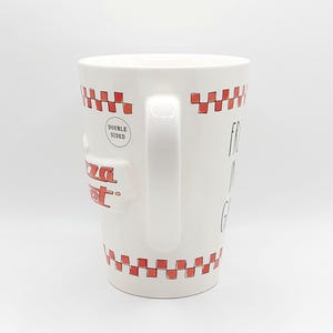 May include: White ceramic mug with a red checkered pattern around the top and bottom. The mug has a handle and the words "Pizza Spot" in red. The mug also has the words "Double Sided" and "Fresh, Hot, & Good" printed on it.