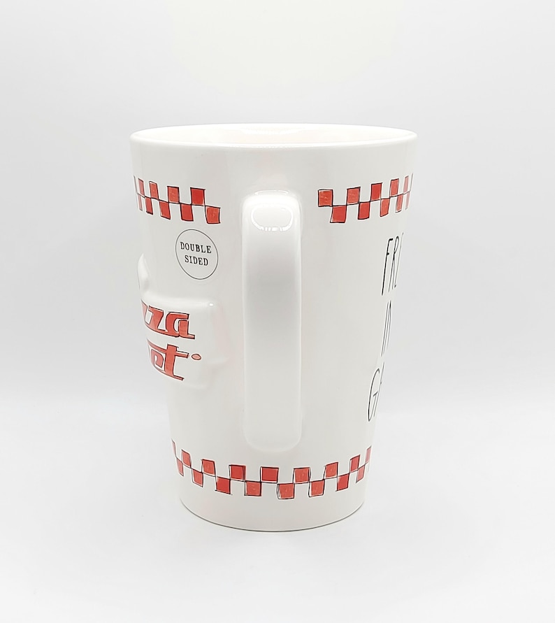 May include: White ceramic mug with a red checkered pattern around the top and bottom. The mug has a handle and the words "Pizza Spot" in red. The mug also has the words "Double Sided" and "Fresh, Hot, & Good" printed on it.