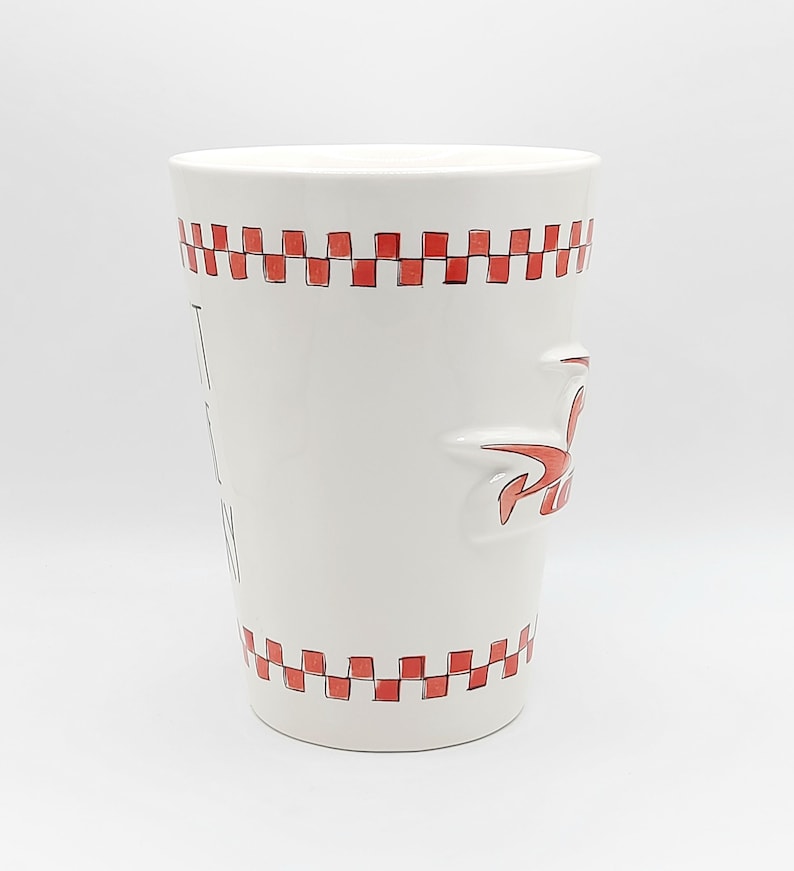 May include: White ceramic mug with red checkered trim and a red stylized logo. The mug has the words "I EAT PIZZA" printed vertically on the side. The mug is cylindrical and has a handle.