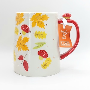 May include: White ceramic mug with a red handle and lid, decorated with autumn leaves and mushrooms. The mug has the text "Painted by Hand" and the brand "LANG" on a tag attached to the handle.