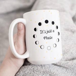 May include: White ceramic mug with a black and white moon phase design and the text "It's just a Phase".