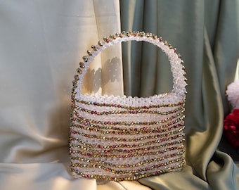 May include: A small, clear beaded handbag with a gold and red iridescent finish. The bag has a top handle and is made of woven beads.